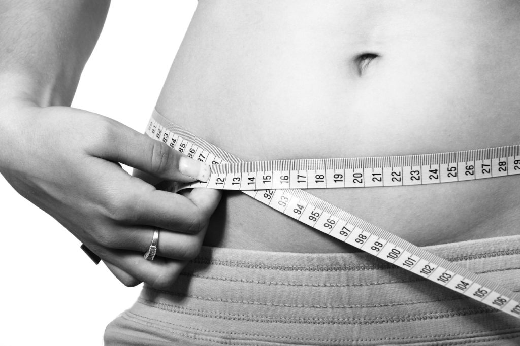 woman measuring her waistline with a measuring tape after laser liposuction michigan