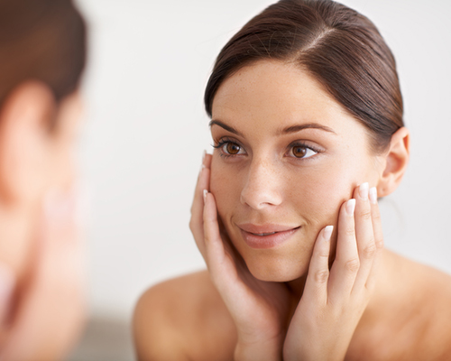 woman looking at her reflection in the mirror with her hands on her face